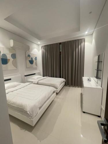 a white bedroom with two beds and a desk at Stella Salalah in Salalah