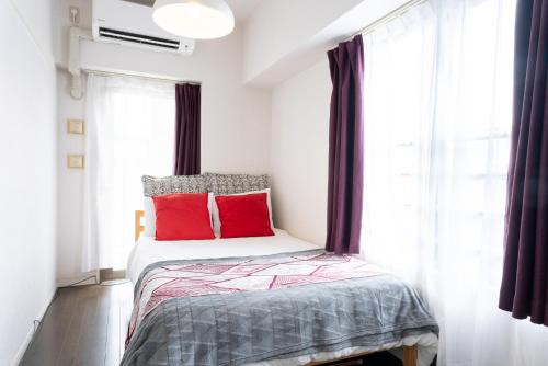a bedroom with a bed with red pillows and a window at Yakuin apartment in Fukuoka