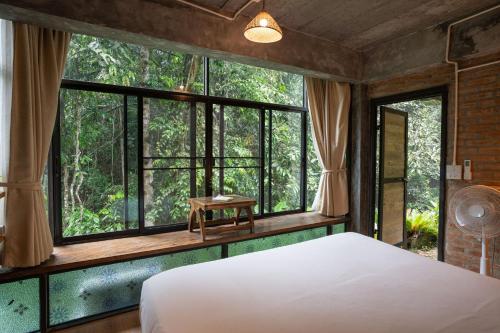 a bedroom with a bed and large windows at Bee Forest in Ban Pok Nai