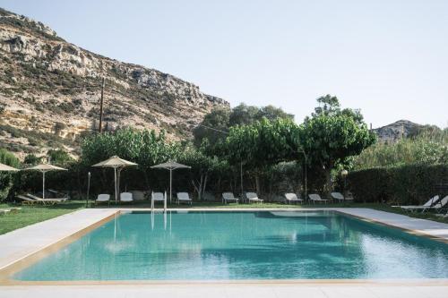 a swimming pool with chairs and umbrellas in front of a mountain at Matala Bay Hotel in Matala