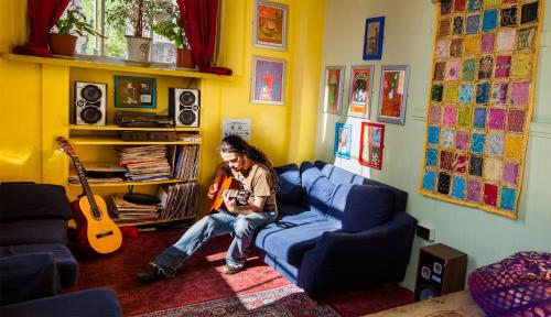 a man sitting on a couch in a living room with a guitar at Castle Rock Hostel - Adults Only in Edinburgh