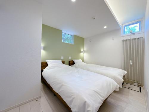 two beds in a bedroom with white walls and a window at GENYA Furano in Nakafurano