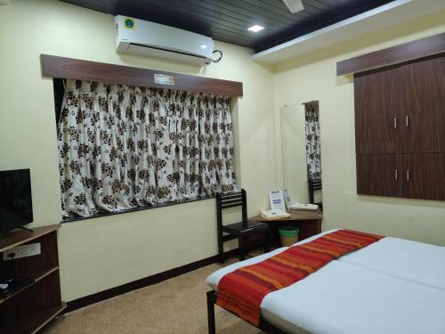 a bedroom with a bed and a tv and a window at Hotel Bakul in Kolhapur