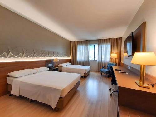 a hotel room with two beds and a desk at Hotel Saint Paul in Sao Jose do Rio Preto