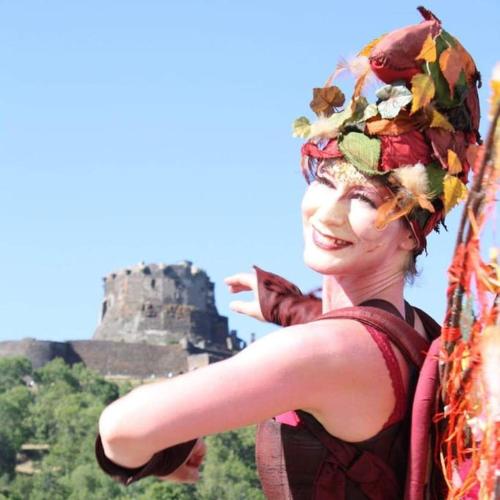 a woman wearing a hat with a castle in the background at Gîte Frimousse les elfes in Murol