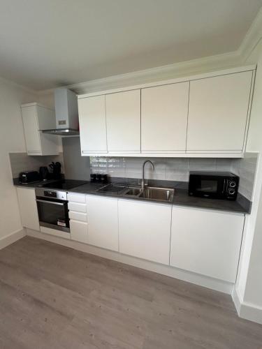 a white kitchen with a sink and a microwave at The Loft and The Den Apartments in Sandown
