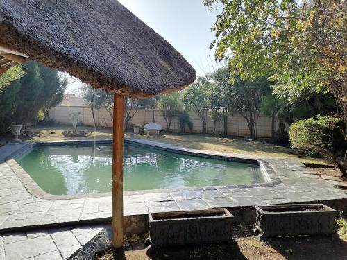 a swimming pool with a straw umbrella next to it at At30 OverNite Stay in Potchefstroom