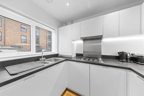 a kitchen with white cabinets and a sink and a window at THE OAK - An Elegant 2 Bedroom House in Dartford - London Zone 8 in Dartford