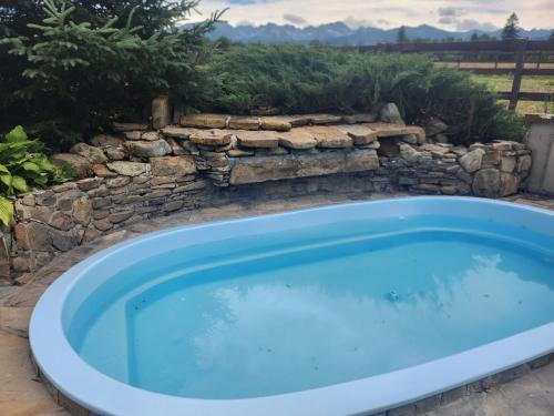 a hot tub in a yard with a stone wall at Osada na Brzyzku in Poronin