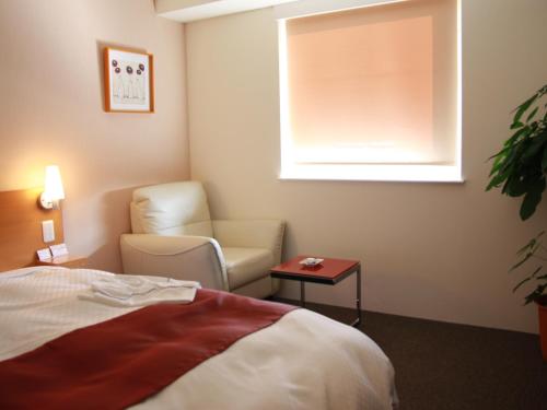 a hotel room with a bed and a chair and a window at Kurume Hotel Esprit in Kurume