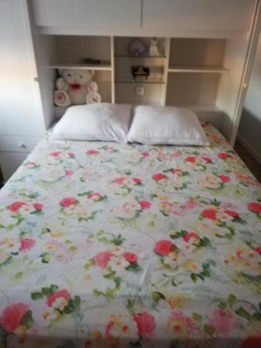 un lit avec un couvre-lit fleuri avec un ours en peluche dessus dans l'établissement Maison neuve au cœur du Golf du Morbihan, à Plougoumelen