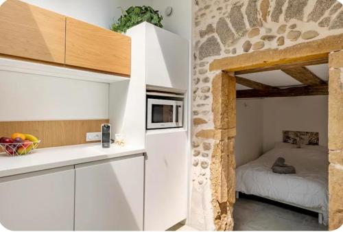 une cuisine avec des armoires blanches et une pièce avec un mur en pierre dans l'établissement Aux Voûtes de Granit - 10 mn Lyon, à Pierre-Bénite