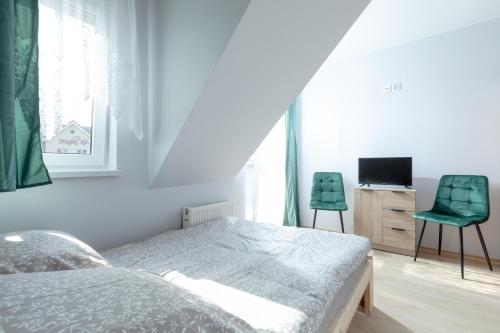 a bedroom with a bed and two green chairs at Pensjonat Jagódka in Trzęsacz