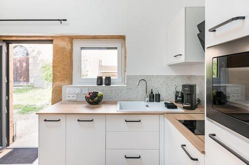 une cuisine avec des armoires blanches, un évier et une fenêtre dans l'établissement Aux Pierres Dorées 10 min centre de Lyon, à Pierre-Bénite