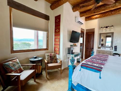 Un dormitorio con una cama y dos sillas y un televisor. en The Grand Hacienda Inn with Breakfast, en Abiquiu