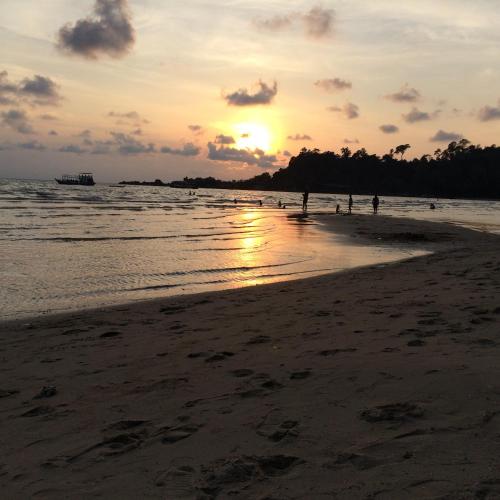 a sunset on a beach with people standing in the water at Elephant & Castle in Ko Chang