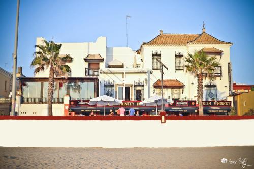 a building with palm trees and tables and umbrellas at Hotel Playa de Regla in Chipiona