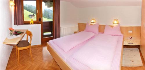 a bedroom with a large bed with pink sheets and a desk at Gästehaus Bergruh in Tux