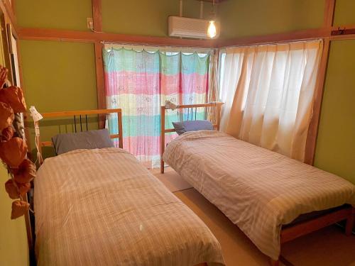 two beds in a room with a window at ゲストハウス千倉のおへそ in Chikura