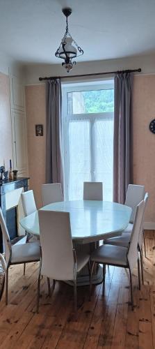 une table à manger avec des chaises blanches et une grande fenêtre dans l'établissement Résidence des Bruyères, Mont Dore, à Mont-Dore