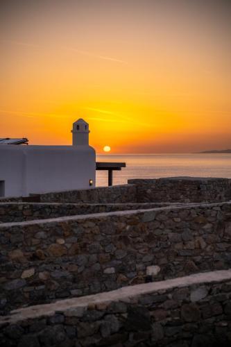 a sunset over the ocean with a lighthouse at Sofia's Bungalows Mykonos in Mýkonos City