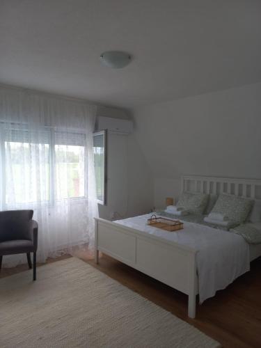 a white bedroom with a bed and a chair at Vikendica Nirvana in Loznica
