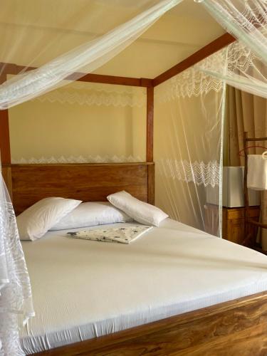 a canopy bed with white sheets and white pillows at Mikoko Beach & Cottages in Bagamoyo