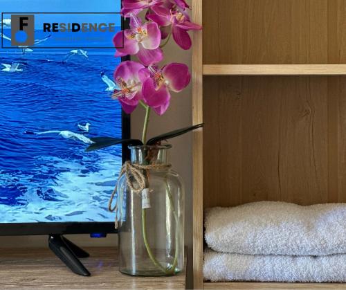 a glass vase with pink flowers in front of a tv at F Residence Transient House in Cabanatuan