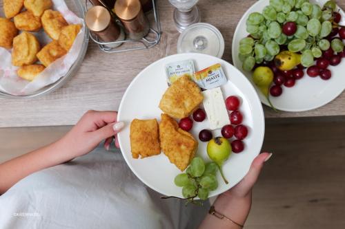 a woman holding a plate of food with grapes and crackers at Comfort Rooms Pogradec in Pogradec