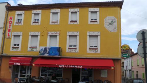 a yellow building with a red awning on a street at Hotel Le Gambetta in Carmaux