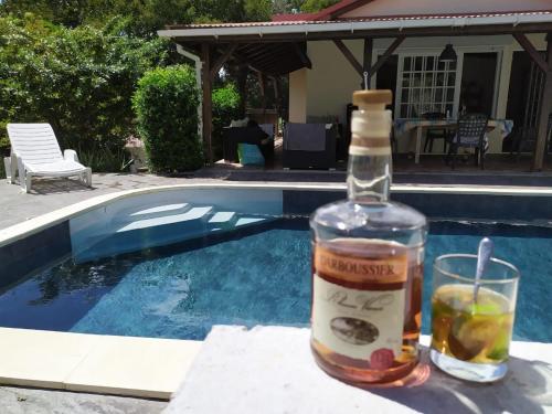 a bottle and a glass next to a swimming pool at Chambres d'hôtes de la villa du Moulin in Le Gosier
