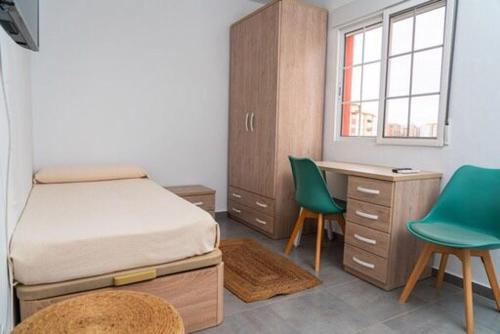 a bedroom with a bed and a desk and two green chairs at Céntrico y luminoso in Huelva