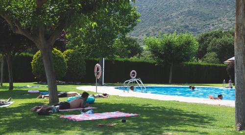 a group of people laying in the grass near a swimming pool at La Noguera Camping in Sant Llorenç de Montgai