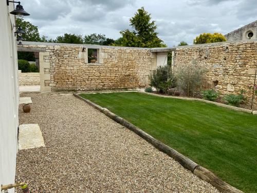 a garden with a stone wall and a lawn at Les gîtes des Lauriers roses Chambre privée Île d Aix in Geay