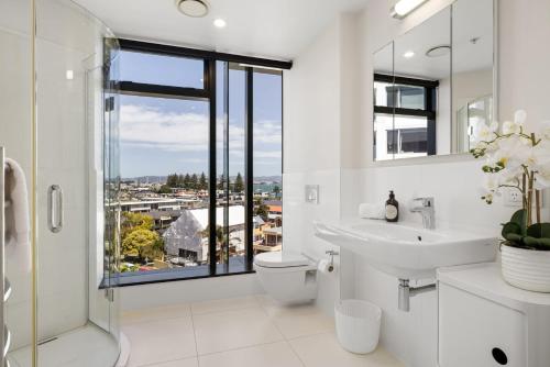 a bathroom with a sink and a toilet and a window at Luxury Ocean & Harbour Views - Heated Pool, Main Beach & Gym in Mount Maunganui
