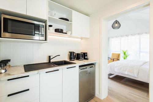 a kitchen with white cabinets and a sink and a bed at Spacious, Breezy Studio Apartment, Moments from Downtown and Beach in Mount Maunganui