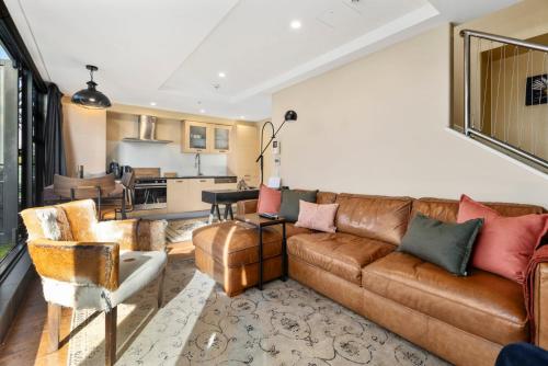 a living room with a brown leather couch at Marvelous Downtown Apartment Moments from Main Beach with Heated Pool, Gym and Parking in Mount Maunganui
