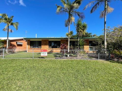 a house with palm trees in front of a fence at Yolanda - Burrum Heads- Beachfront - 3BR- Aircon in Burrum Heads