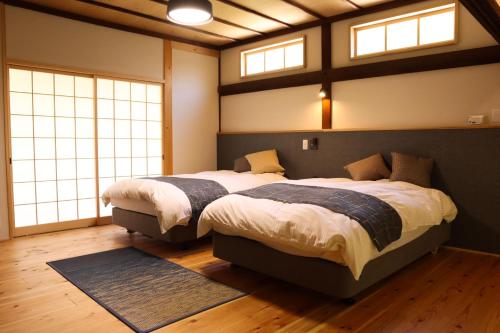 two beds in a bedroom with two windows at まほろの宿 - 明日香村のリノベーション古民家一棟貸し in Asuka