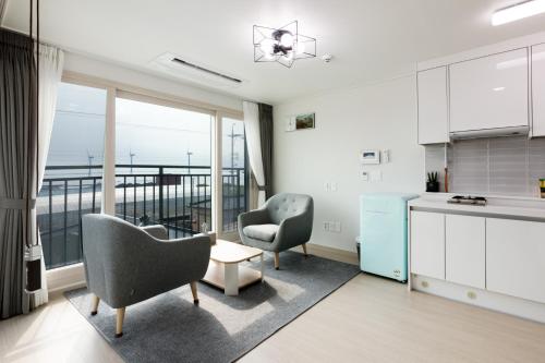 a living room with two chairs and a kitchen with a view at Jemibareut Pension in Jeju