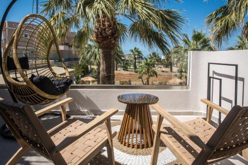 a patio with two chairs and a table and a palm tree at Ammos Boutique Apartments & Suites in Malia