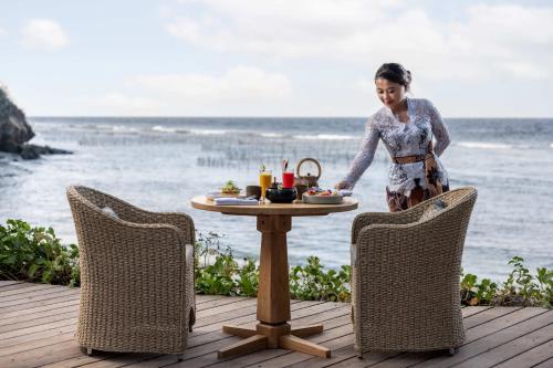 een vrouw die op een terras staat met een tafel met eten bij Semaya Beach Resort in Nusa Penida