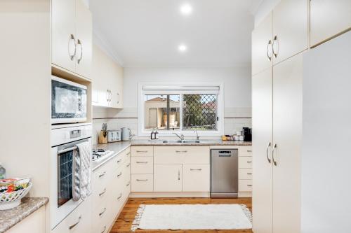 a white kitchen with white cabinets and a window at A Charming, Central & Family Friendly Cottage in Toowoomba