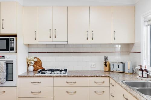 a white kitchen with white cabinets and a sink at A Charming, Central & Family Friendly Cottage in Toowoomba