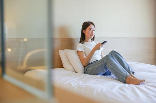 a woman sitting on a bed looking at her cell phone at From H The Best Hotel Jeju Seongsan in Seogwipo