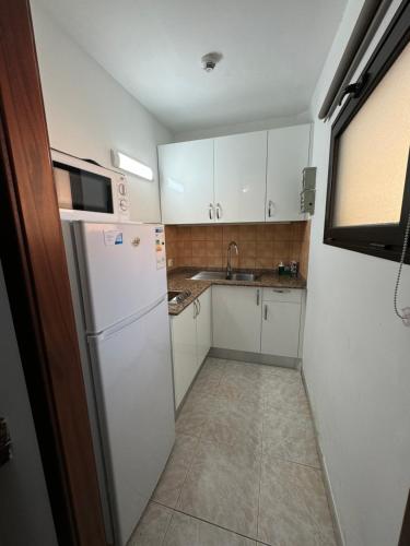 a small kitchen with white cabinets and a refrigerator at Guinea Apartment in Playa del Ingles