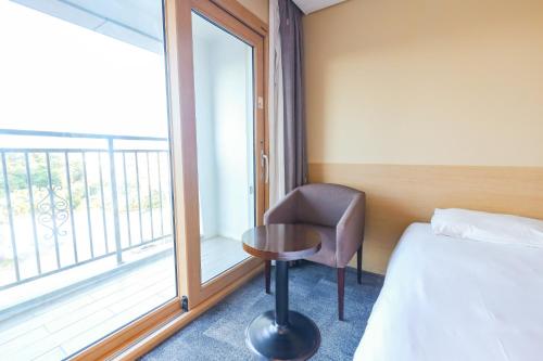 a bedroom with a bed and a chair and a window at From H The Best Hotel Jeju Seongsan in Seogwipo