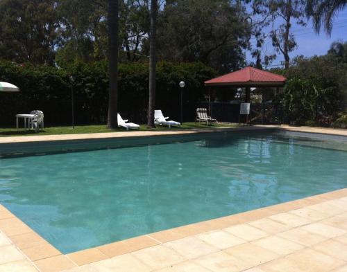 a large blue swimming pool with chairs and a gazebo at Edgewater Holiday Park in Port Macquarie