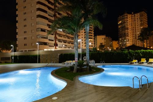 a swimming pool at night with a palm tree and buildings at Flamenco Ambar Luxury Apartment 15 Planta in Calpe