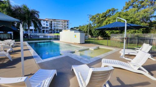 a swimming pool with white chairs and an umbrella at L'Amor Holiday Apartments in Yeppoon